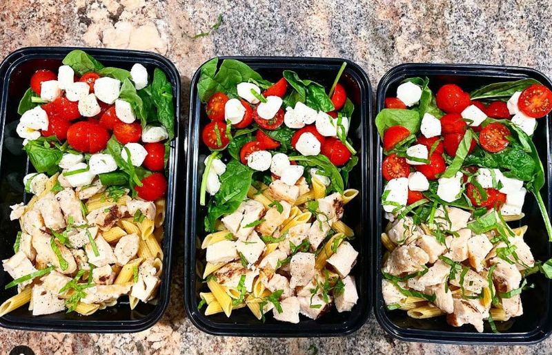Three black plastic containers filled with Caprese salad ingredients