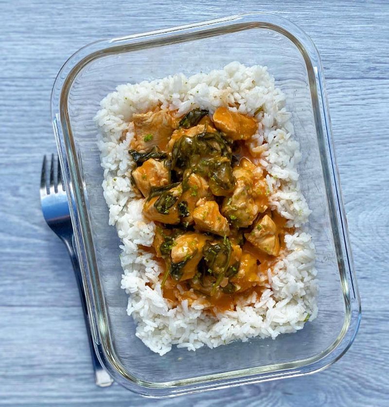 Glass bowl holding rice topped with coconut chicken stew and a fork