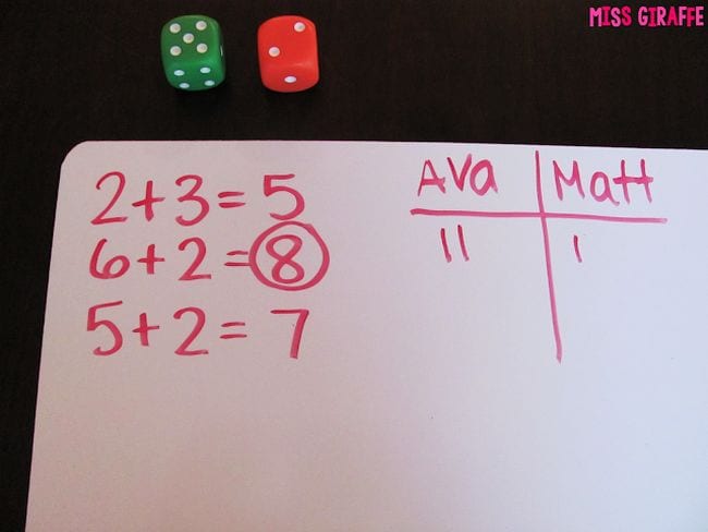 Pair of dice with a whiteboard with addition problems written on it, used by kids playing first grade math games