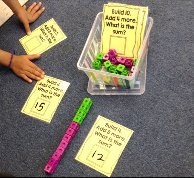 Math cubes with printed cards saying "Build 4. Add 8 more. What is the sum?" and child using them to play first grade math games