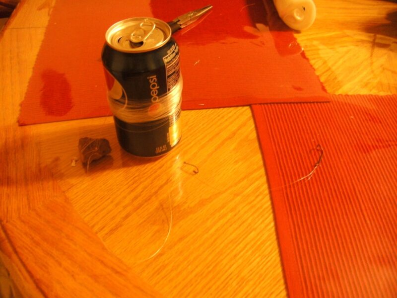 A soda can has cord wrapped around it and is sitting next to a rock and a hook.