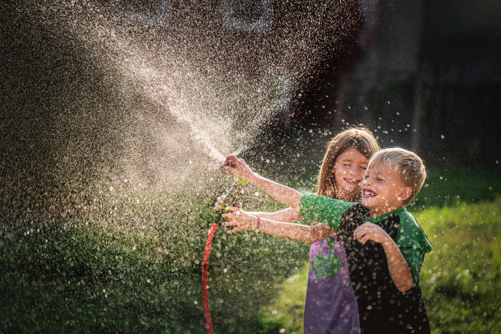 Happy little boy and girl playing with garden hose. Summer camp activities often include waterplay.