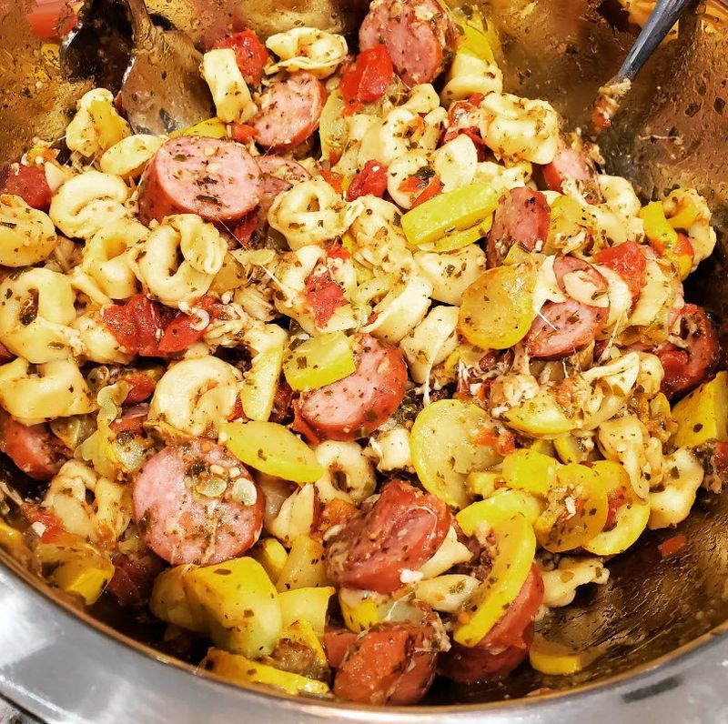Pan containing tortellini, sausage, and peppers in a pesto sauce