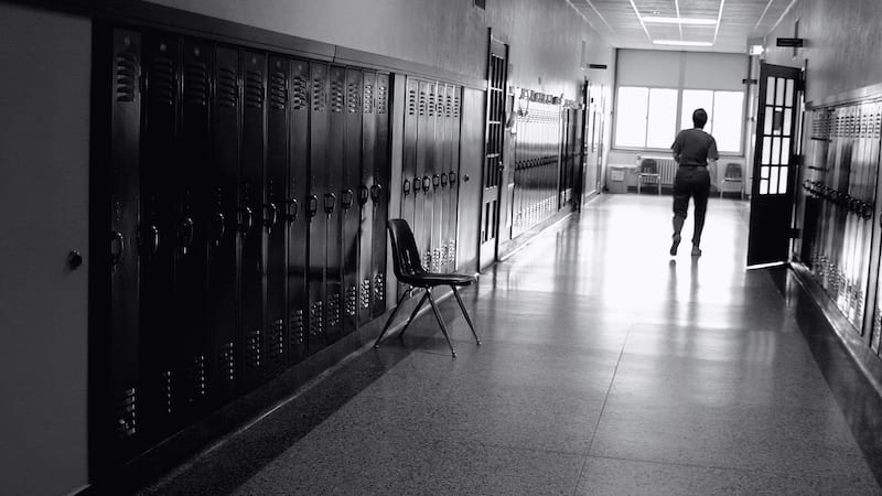 Black and white photo of a teacher in a hallway with lockers--let's stop teacher blame